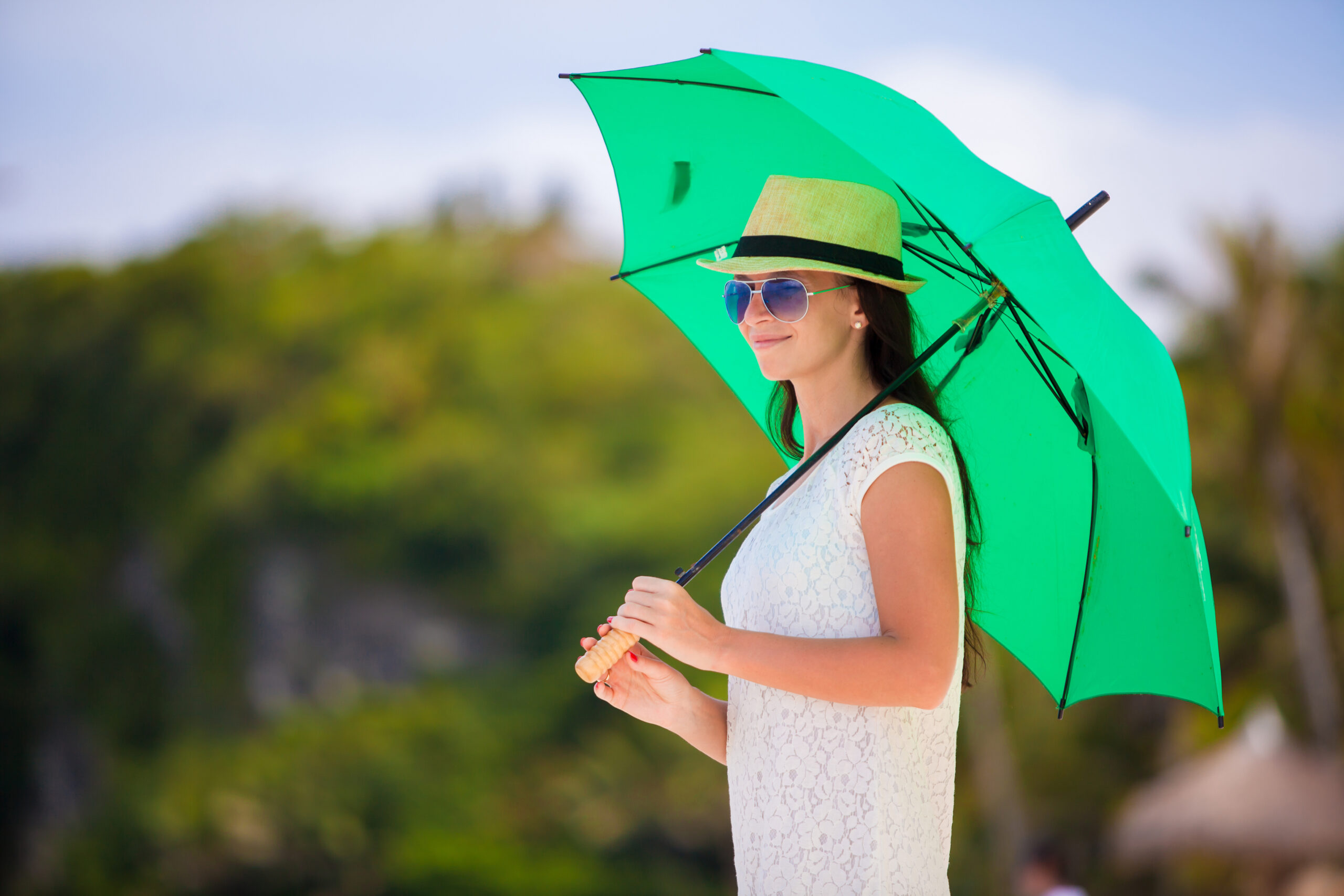 Young girl with green umbrella on white beach